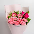 Pink gerbera daisies and carnations with green foliage in soft pink wrapping paper