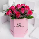 Pink hexagonal box with 12 vibrant hot pink roses and green foliage arrangement