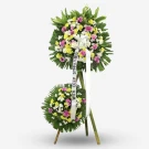 Two-tier standing funeral wreath with pink, white, and yellow flowers on green foliage