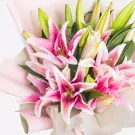 Vibrant pink and white lilies with green buds wrapped in soft pale pink paper
