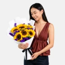 Bright bouquet of yellow sunflowers with purple statice flowers wrapped in white paper