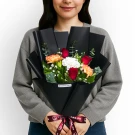 Woman holding black-wrapped bouquet with red roses, orange carnations, and white flowers