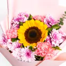 Vibrant sunflower surrounded by pink carnations and magenta chrysanthemums in pink wrapping
