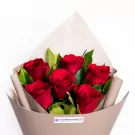 Red roses bouquet with green leaves wrapped in beige paper