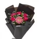 Vibrant pink gerberas and baby's breath arranged in black wrapped bouquet