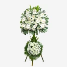 White flower sympathy standing spray with lilies, daisies, and green foliage