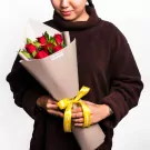Red roses bouquet with green leaves wrapped in cream paper with yellow ribbon