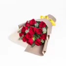 Red roses bouquet with greenery wrapped in beige and cream paper with yellow bow