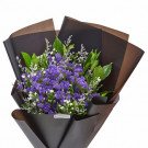 Purple and white flowers with green foliage in dark brown paper wrapping
