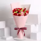 Pink wrapped bouquet with red roses, pink carnations, and green foliage with burgundy ribbon