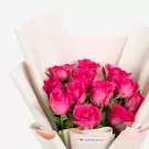Vibrant pink roses bouquet wrapped in white paper with green stems and leaves