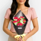 Woman holding bouquet of red carnations and white flowers in black wrapper with yellow ribbon