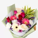 Colorful bouquet with red roses, pink gerberas, white flowers, purple accents and green foliage in soft wrapping
