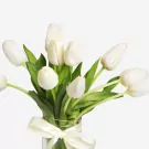 White tulips bouquet with green stems in clear vase with white ribbon