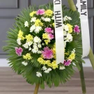 Vibrant sympathy wreath with yellow, white, and pink daisies and greenery