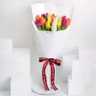 Vibrant assorted tulips in yellow, orange, pink, and purple wrapped in white paper with red ribbon