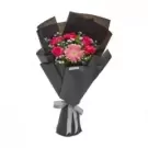 Vibrant pink and red flowers arranged in black wrapping with gray ribbon bow