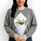 White rose bouquet with greenery in lavender wrapping paper held by woman in gray sweater