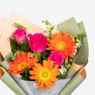 Vibrant bouquet with orange gerberas, pink roses, and white filler flowers in green wrapping