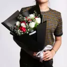 Person holding black wrapped bouquet with white and red roses, greenery accents