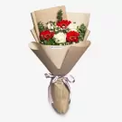 Elegant bouquet of red gerberas, white rose, and white baby's breath in kraft paper wrapper