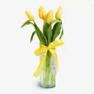 Five yellow tulips with green stems in a clear glass vase with yellow ribbon