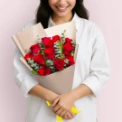 Woman holding bouquet of 12 red roses with eucalyptus greenery wrapped in cream paper