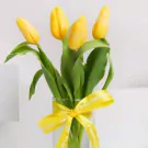 Five yellow tulips with green stems in a white vase with yellow ribbon bow