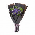 Purple flowers with green foliage in dark brown paper wrapping with purple ribbon