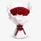 Luxurious bouquet of 100 red roses wrapped in white paper with burgundy ribbon bow