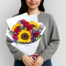 Vibrant bouquet with sunflowers, red roses, purple statice, and white baby's breath in white wrapping