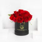 Red roses in black cylindrical vase with gold branding, elegant floral arrangement
