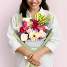 Colorful bouquet with red roses, pink gerberas, white daisies, and purple statice wrapped in green paper