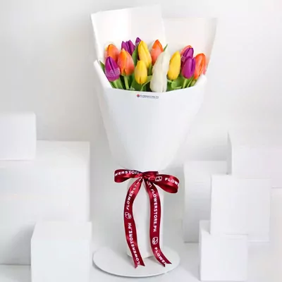 Vibrant assorted tulips in yellow, orange, pink, and purple wrapped in white paper with red ribbon