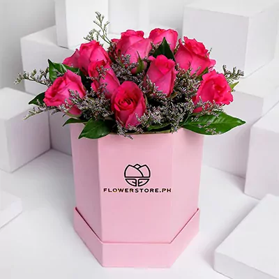 Pink hexagonal box with 12 vibrant hot pink roses and green foliage arrangement