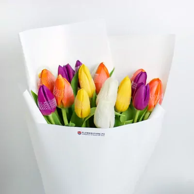 Vibrant assorted tulips in orange, yellow, and purple wrapped in white paper bouquet