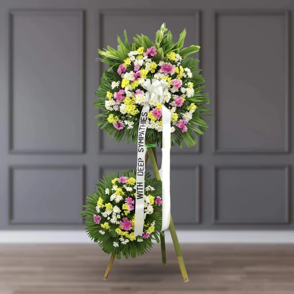 Two-tier funeral standing spray with white, pink, and yellow flowers on easel