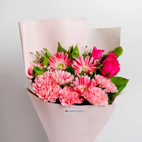 Pink gerbera daisies and carnations with green foliage in soft pink wrapping paper