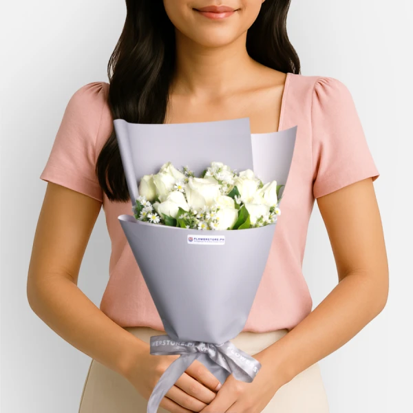 White roses bouquet with green foliage in lavender wrapper, held by woman in pink shirt