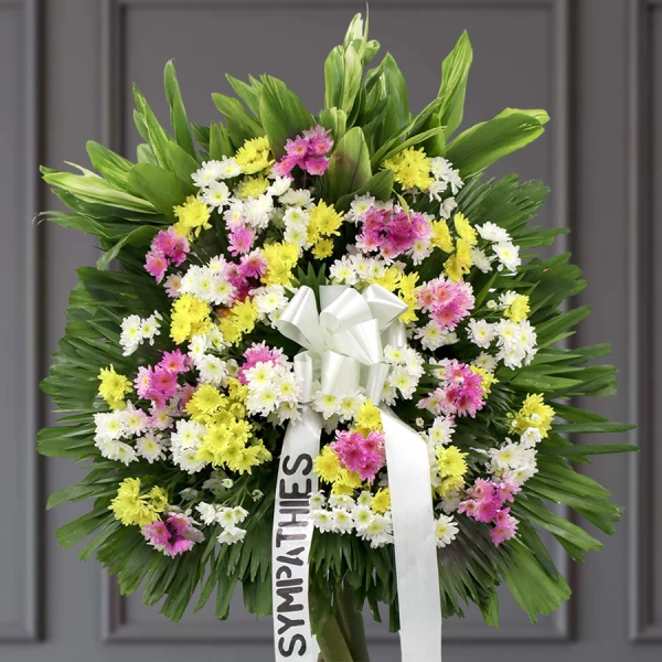 Sympathy wreath with pink, yellow, and white daisies on green foliage background