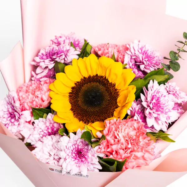 Vibrant sunflower surrounded by pink carnations and magenta chrysanthemums in pink wrapping