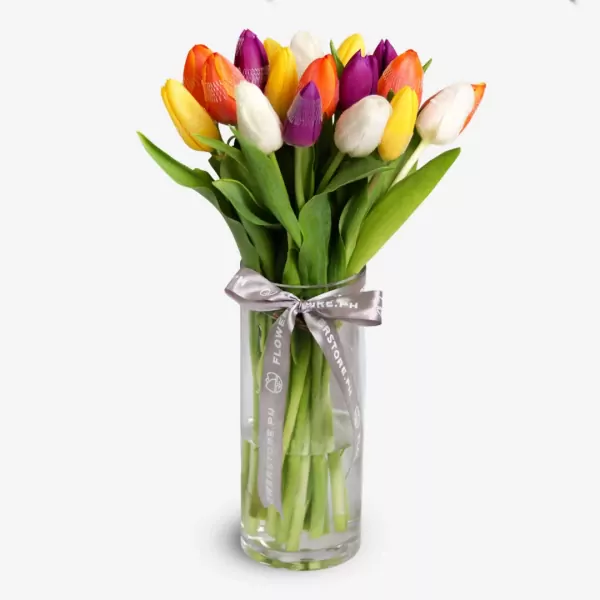 Colorful assorted tulips in glass vase with purple ribbon bow arrangement