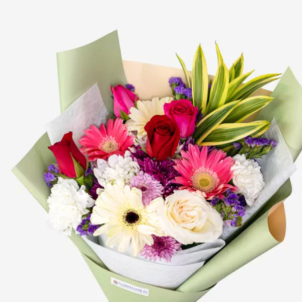 Colorful bouquet with red roses, pink gerberas, white flowers, purple accents and green foliage in soft wrapping