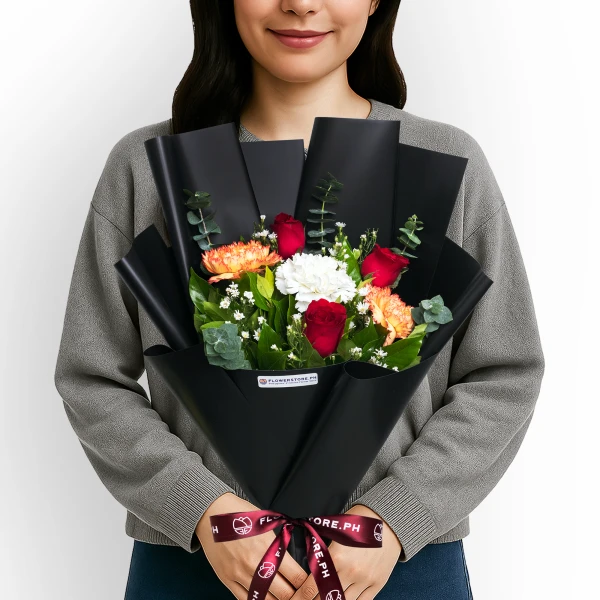 Woman holding black-wrapped bouquet with red roses, orange carnations, and white flowers