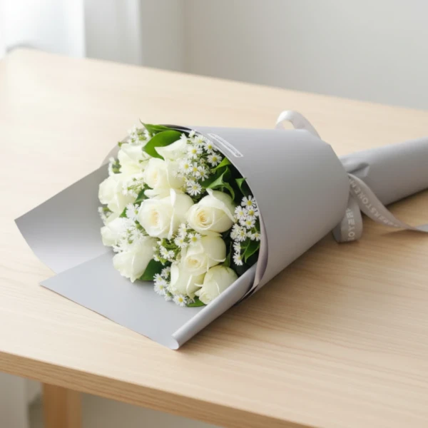 White roses bouquet with baby's breath filler wrapped in white paper on wooden table