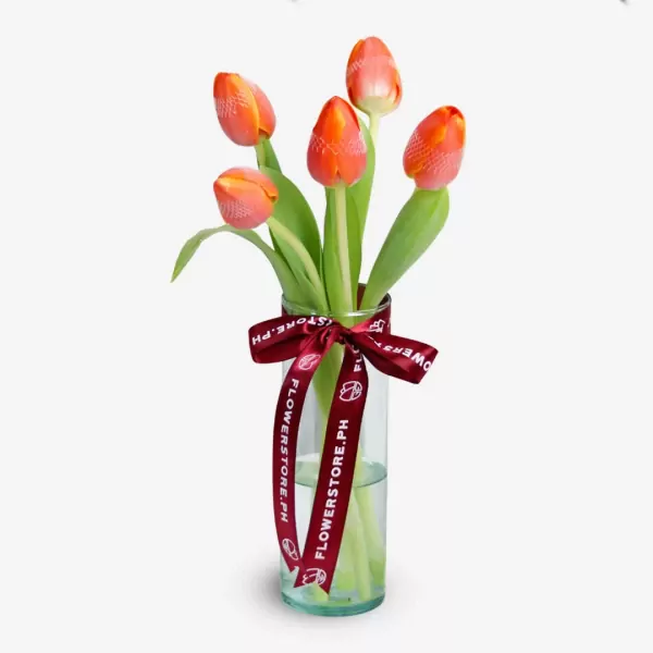 Five red-orange tulips with green stems in a clear vase with burgundy ribbon