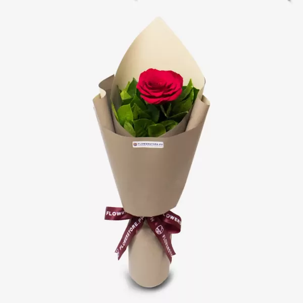 Single red rose with green foliage wrapped in beige paper with burgundy ribbon bow