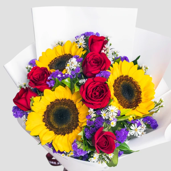 Vibrant bouquet with yellow sunflowers, red roses, purple flowers, and white daisies in white wrap