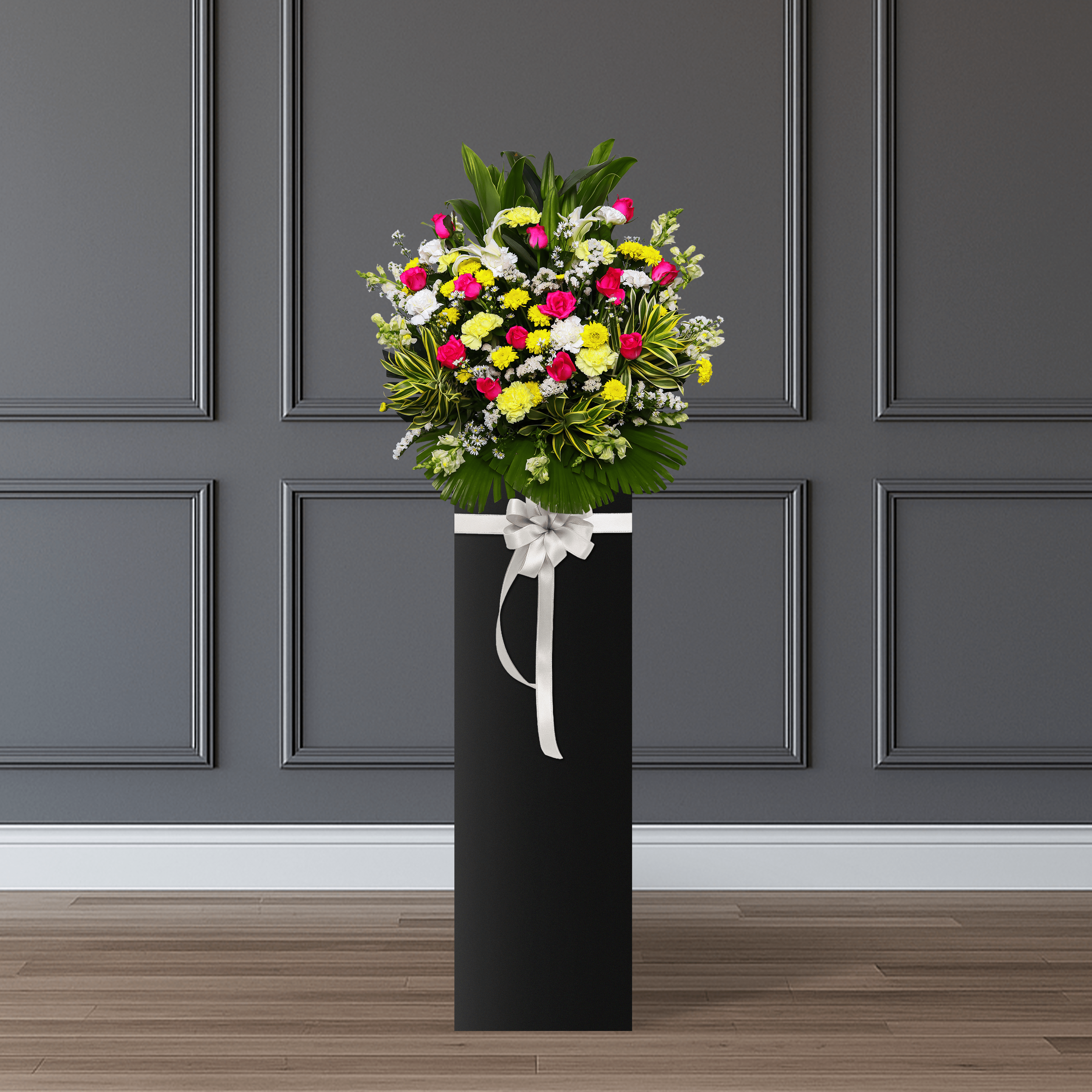This arrangement consists of pink roses, yellow carnations, white carnations, yellow mums, white snapdragon, aster, and palm leaves.