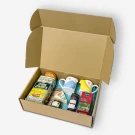 Open gift box filled with crackers, cheese, jam, tea, and two novelty mugs.